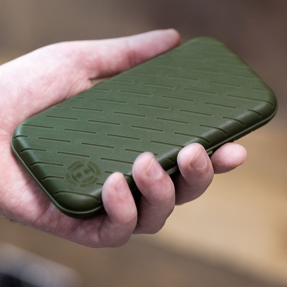 Eine Hand hält ein schlankes, grünes Etui. Das Etui hat ein strukturiertes Muster und ein rundes Logo in der Ecke.