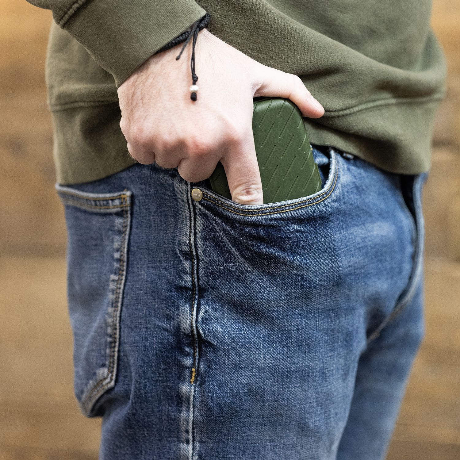 Harrows Slimcase Dart Case Eine Person steckt ein grünes Etui in die vordere Hosentasche einer Jeans. Das Etui hat eine strukturierte Oberfläche und passt gut in die Tasche.