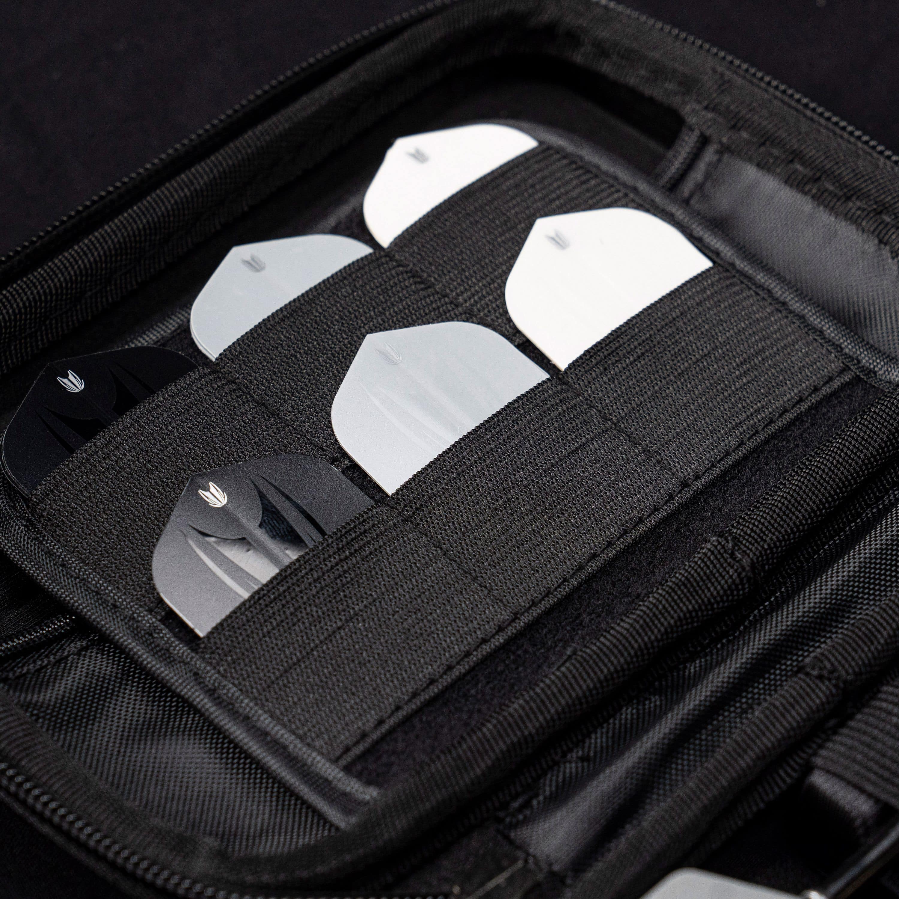Takoma XL Ghost Series Raymond Van Barneveld dart case Das Bild zeigt das „Target Takoma Bolide XL Dartcase“, das mehrere Dart-Flights in schwarzen und weißen Farben organisiert aufbewahrt. Die Flights sind sicher in elastischen Halterungen im Inneren des schwarzen Etuis verstaut.