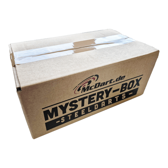 McDart Mystery Box - Steeldarts Auf dem Bild ist ein Karton mit der Aufschrift "McDart.de Mystery-Box - Steeldarts" zu sehen. Die Box ist oben mit Klebeband verschlossen.