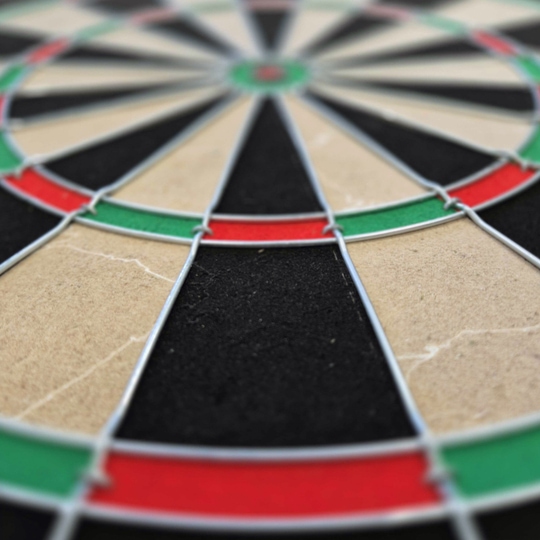 Das Bild zeigt eine Nahaufnahme eines Steeldartboards mit schwarz, beige, rot und grün markierten Segmenten. Besonders gut zu erkennen sind die Drähte, die die Felder voneinander trennen.