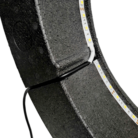 Bulls NL Lumo Light Surround lighting system Das Bild zeigt das „Bulls NL Lumo Light Surround Beleuchtungssystem“ mit LED-Leuchtstreifen auf einer schwarzen, strukturierten Oberfläche. Ein Kabel ist ebenfalls an das Beleuchtungssystem angeschlossen.
